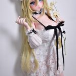 Life-sized anime-style doll with long blonde hair in a white lace off-shoulder dress, holding pale flowers against a plain background.