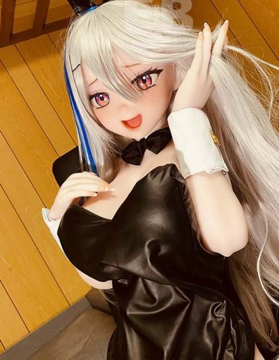 Cosplayer in a black satin bunny outfit with white gloves and long silver hair, black ears, posing playfully with a finger to her lips and tongue out.