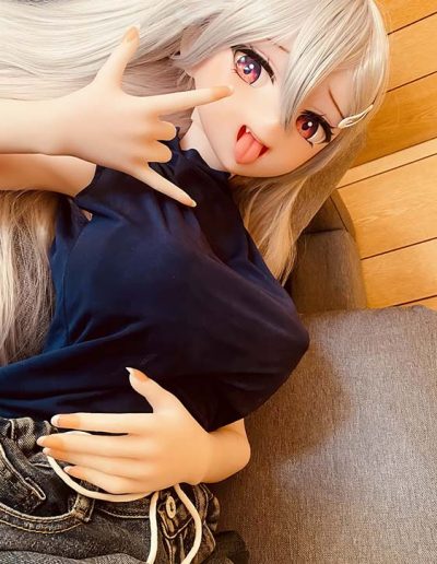 Anime-style doll with long silver hair lying on a gray couch, sticking out tongue and making a rock-on hand gesture.