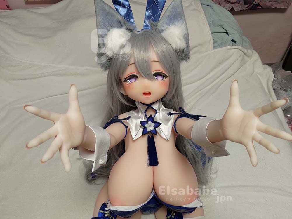 Cosplay doll with gray hair and cat ears sits on a bed, arms extended toward the camera in a blue and white outfit with tassels and flower accents.