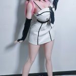 Life-size pink-haired anime-style doll in a white and black mini dress, standing against a white wall
