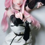Cosplay doll with pink hair and elf ears, wearing a white and black dress, posing with hands reaching toward the camera.