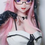 Life-size anime-style doll with pink hair, elf ears, glasses, and a white-and-black outfit posing with hand near the chin.
