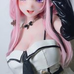Life-like pink-haired anime doll with elf ears and purple eyes, wearing a white and black corset-style outfit and black accessories, posing playfully.