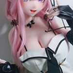 Anime-style pink-haired cosplay doll with elf ears wearing a white lace corset dress and black gloves, smiling at the camera.