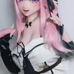 Cosplay doll with pink hair and elf-like ears, posing with hands in her hair, wearing a white and black outfit with a beaded necklace.